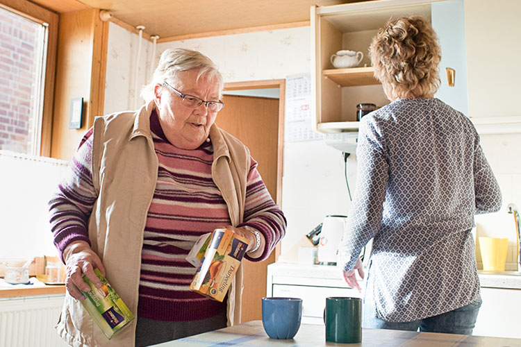 Eine Ältere Dame steht mit ihrer Pflegerin in der Küche und bereitet Tee zu