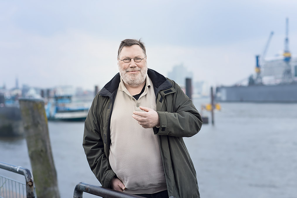 Mann mit Bart und Brille steht am Hamburger Hafen und lächelt in die Kamera