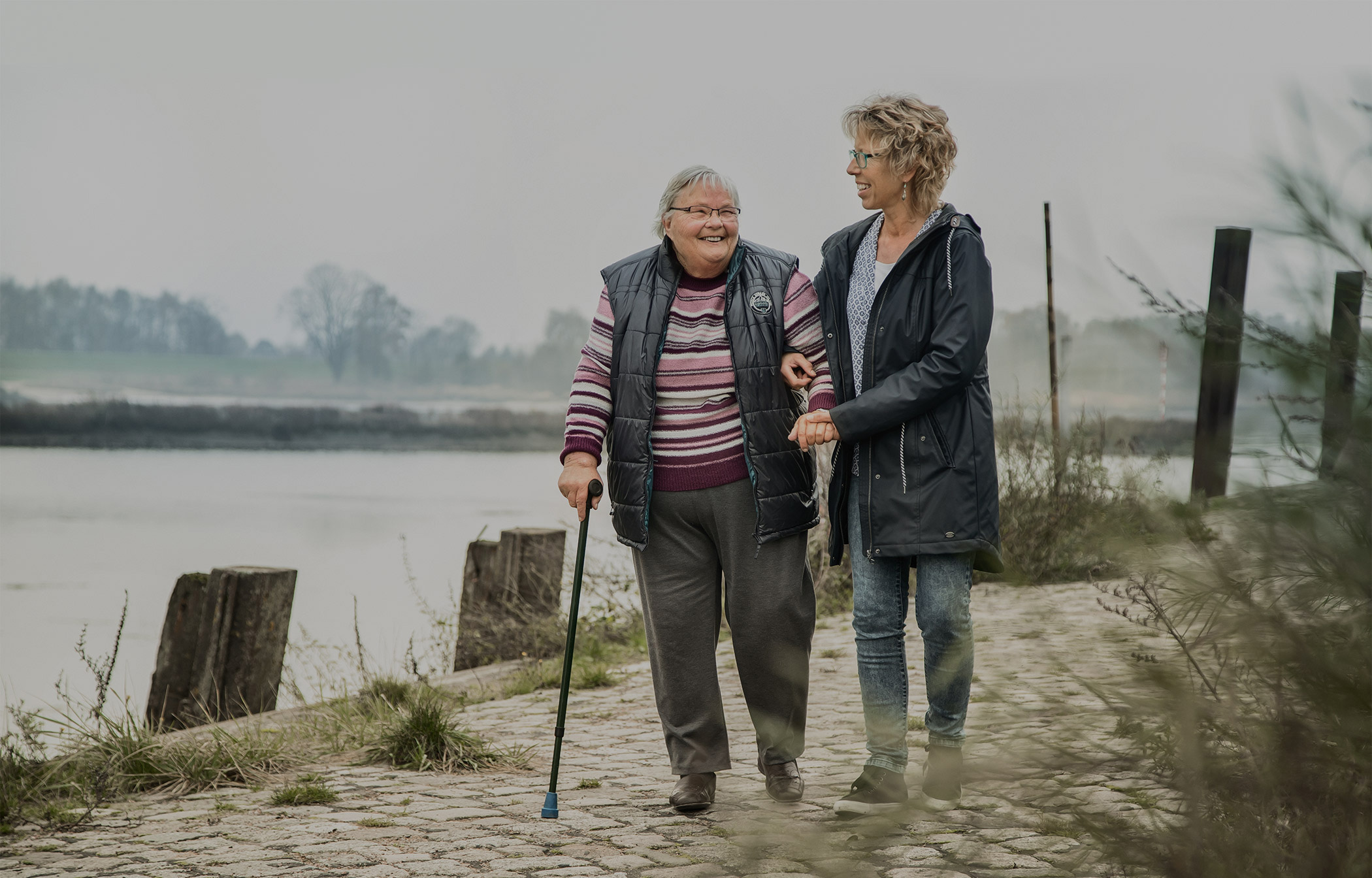 Frau spaziert mit ihrer Pflegerin an der Elbe entlang