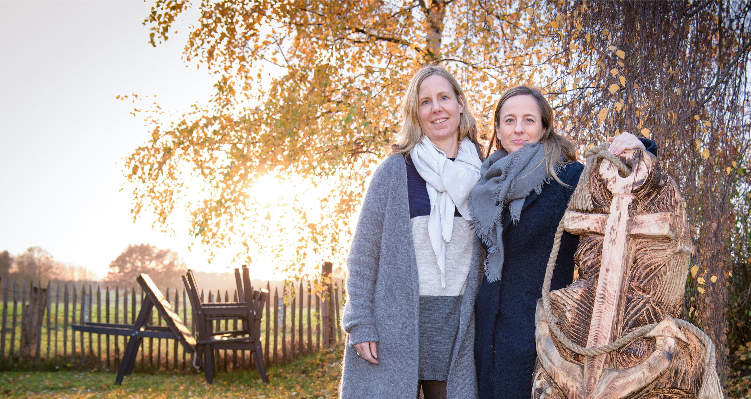 Zwei Frauen stehen neben einem Holzanker auf dem das Wort KidsAnker steht und lächeln in die Kamera.